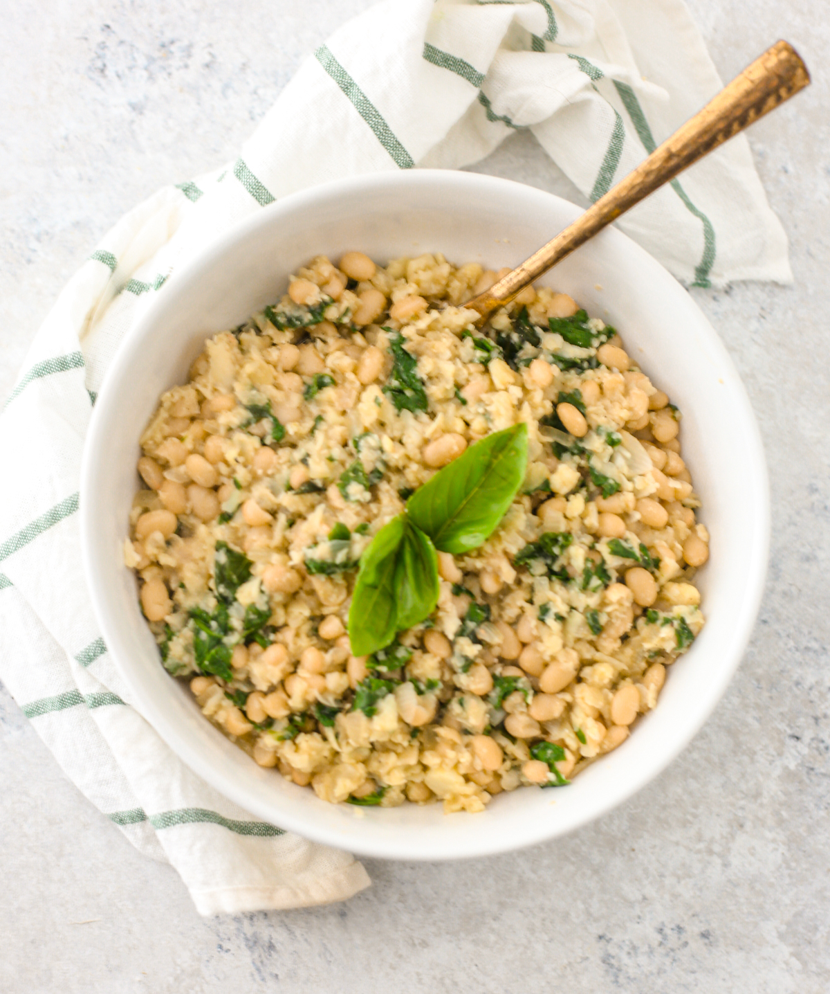 Cauliflower rice and white navy beans risotto in almond sauce topped with basil leaves served in white bowl. 